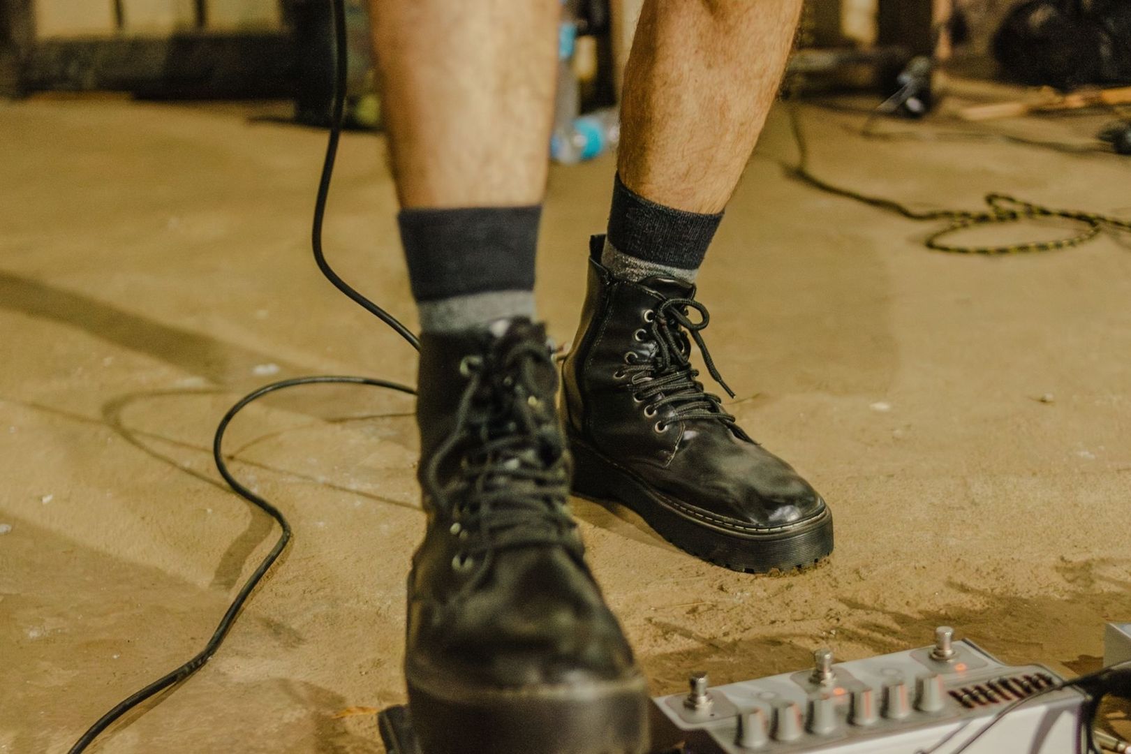 Schwarze Stiefel neben Kabeln und einem Effektgerät auf einem Bühnenboden